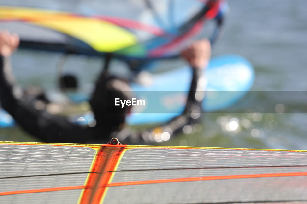 Close-up of windsurfing board by man in sea