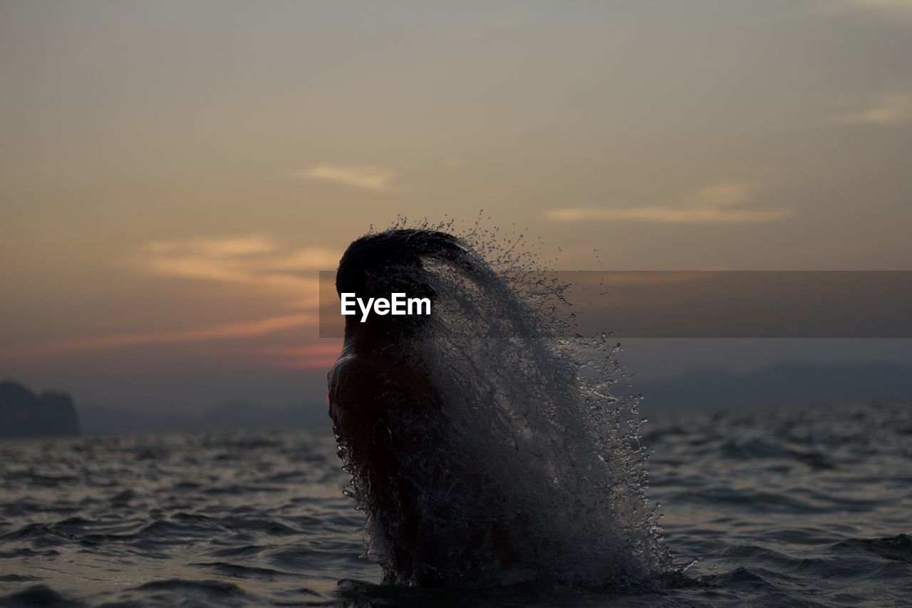 Silhouette man splashing water with hair in sea at sunset