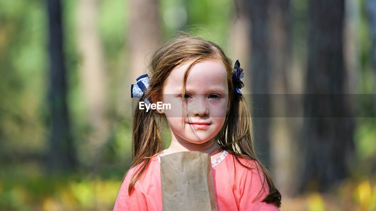 Close-up portrait of girl with paper bag against trees in forest