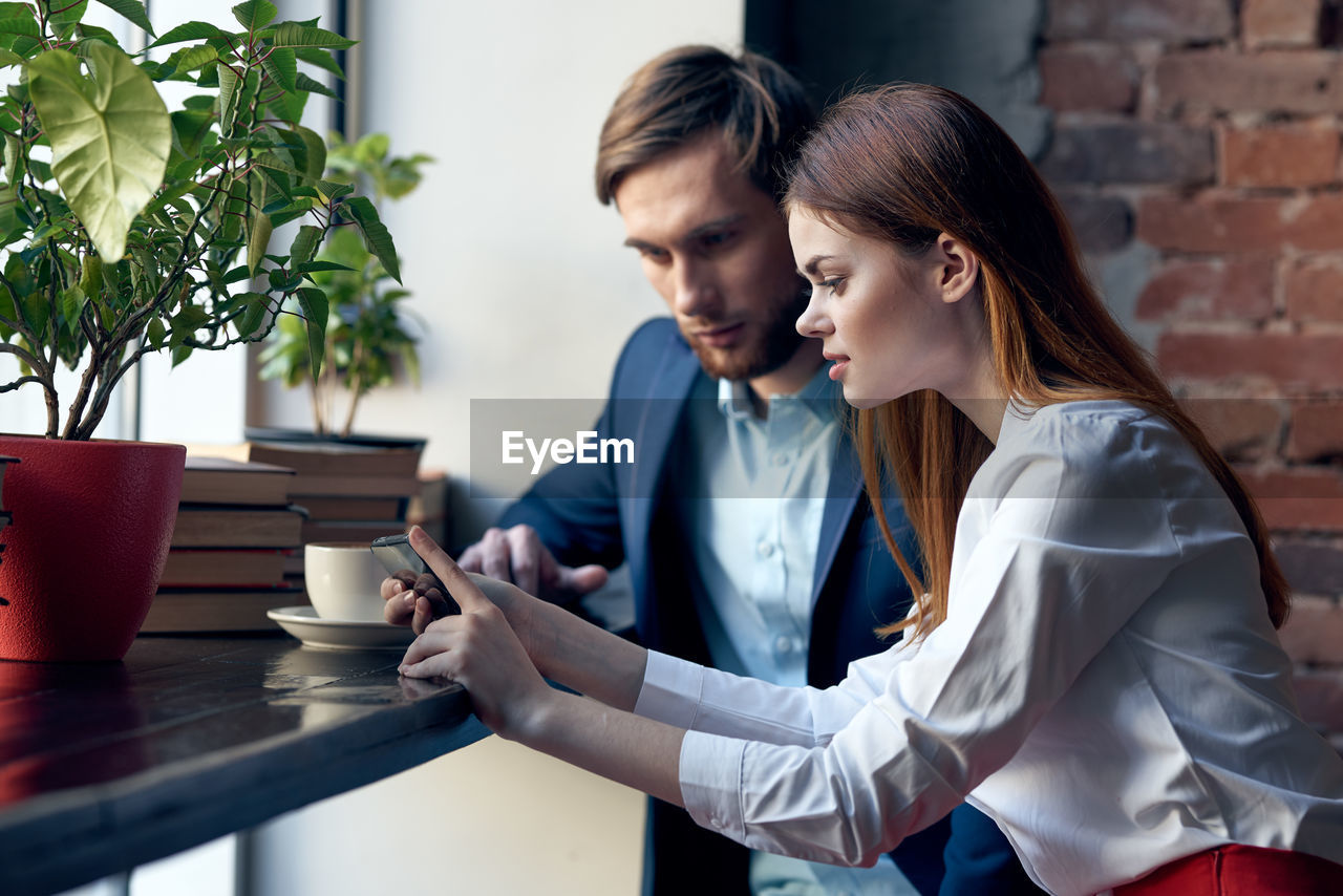 Young businesswoman and businessman looking at mobile phone at cafe