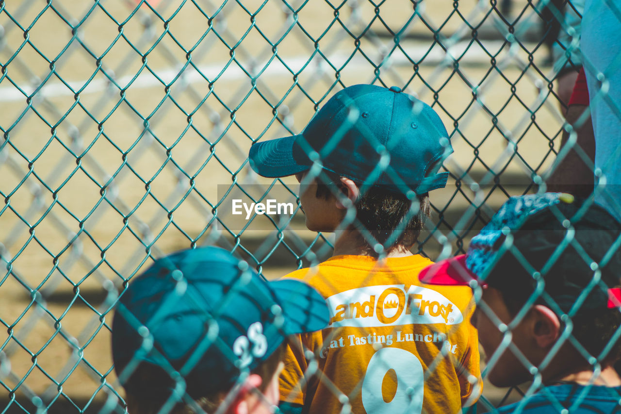 REAR VIEW OF MAN SEEN THROUGH CHAINLINK FENCE AGAINST BLURRED BACKGROUND