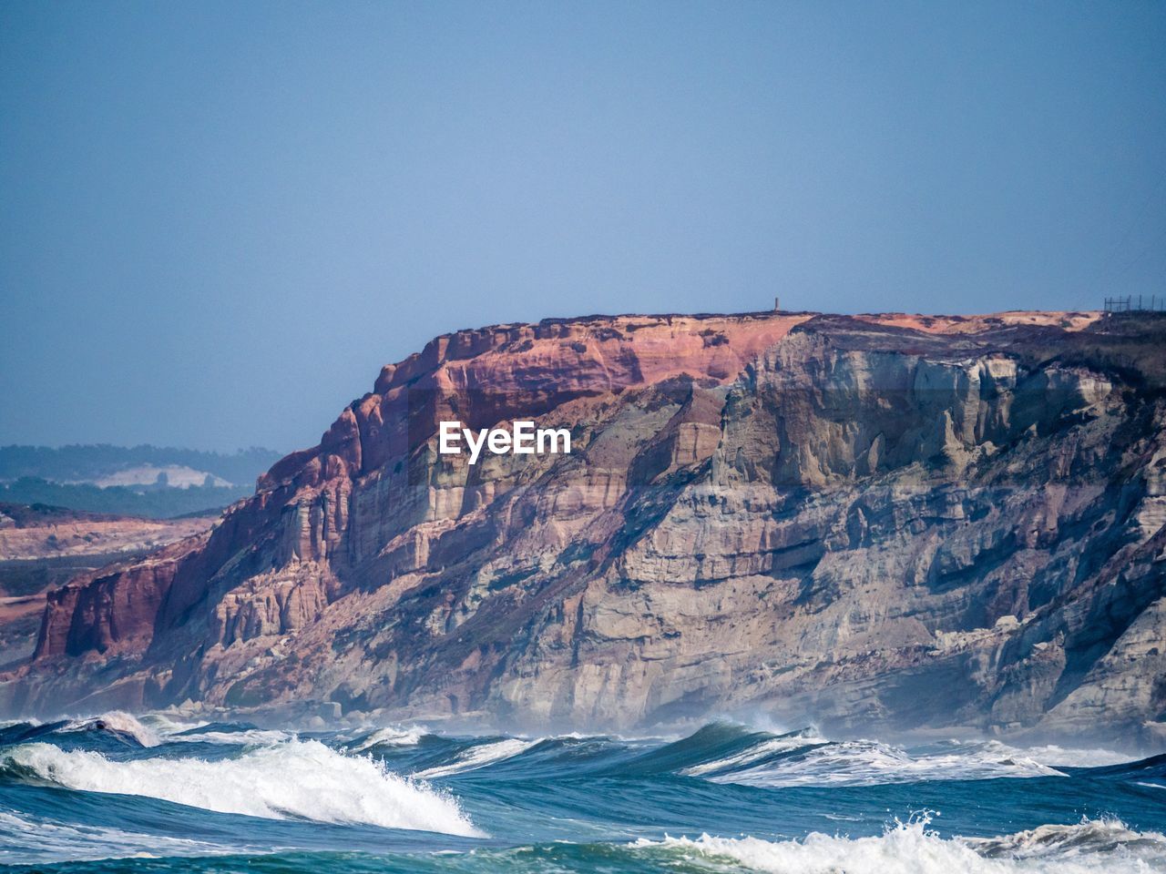 Scenic view of cliff by sea against clear sky