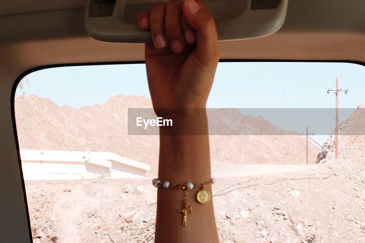 Cropped woman hand in car against mountains