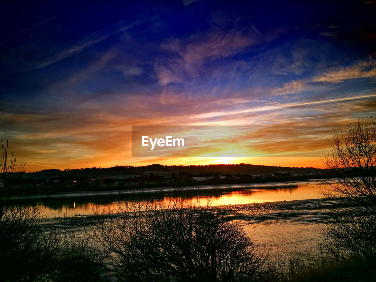 SCENIC VIEW OF LAKE AGAINST DRAMATIC SKY AT SUNSET