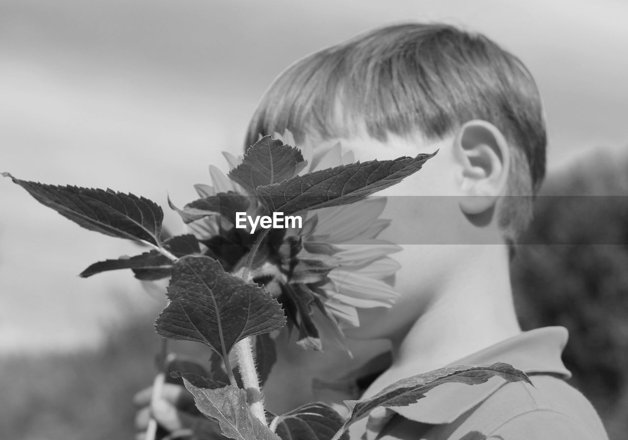 Close-up of boy with sunflower against sky