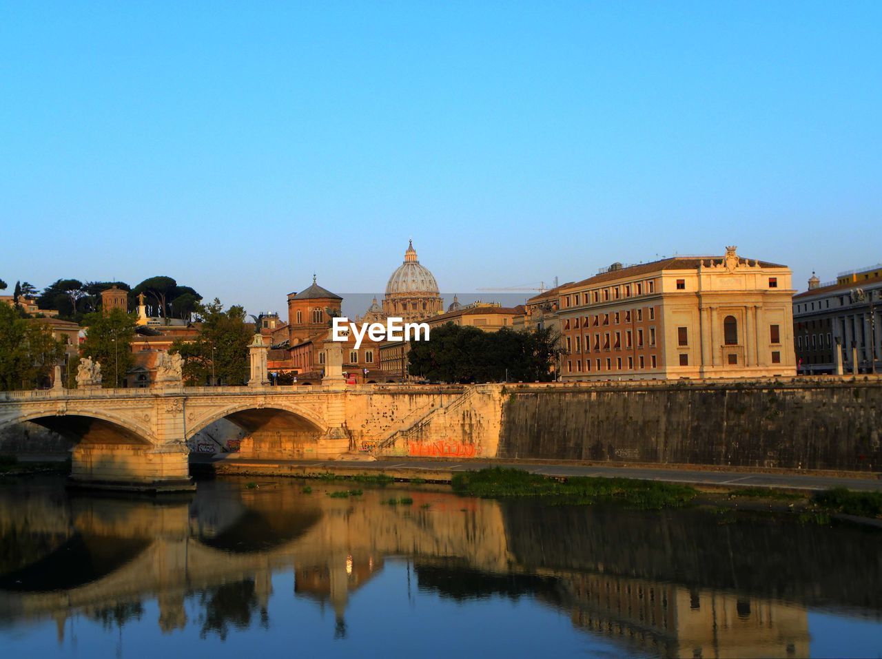 Bridge over river by st peter basilica against clear blue sky in city