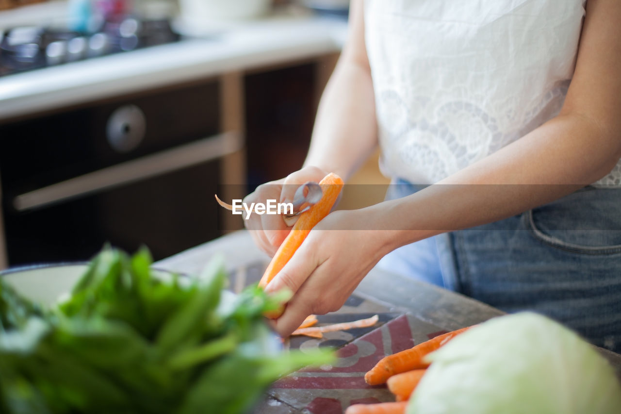 Midsection of woman peeling carrot in kitchen