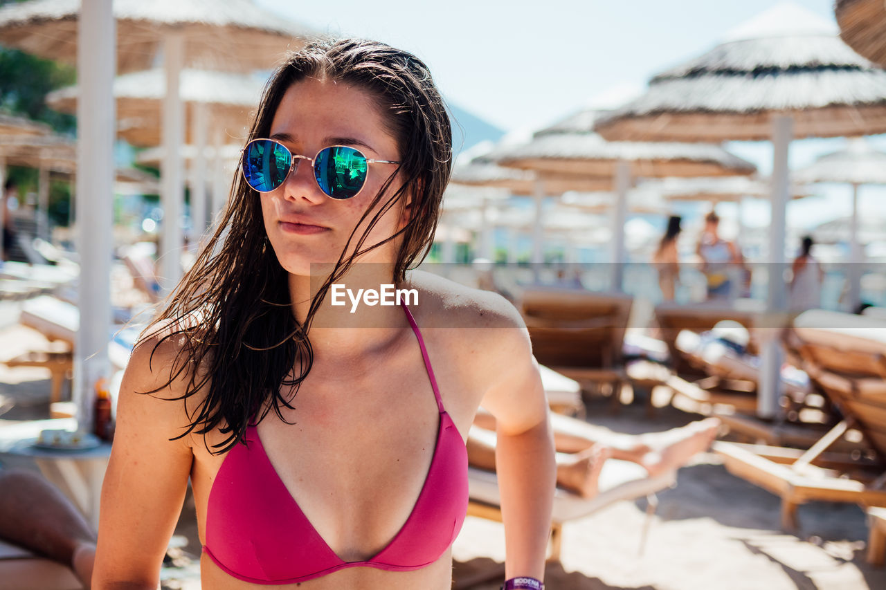 Close-up of young woman in bikini wearing sunglasses at beach