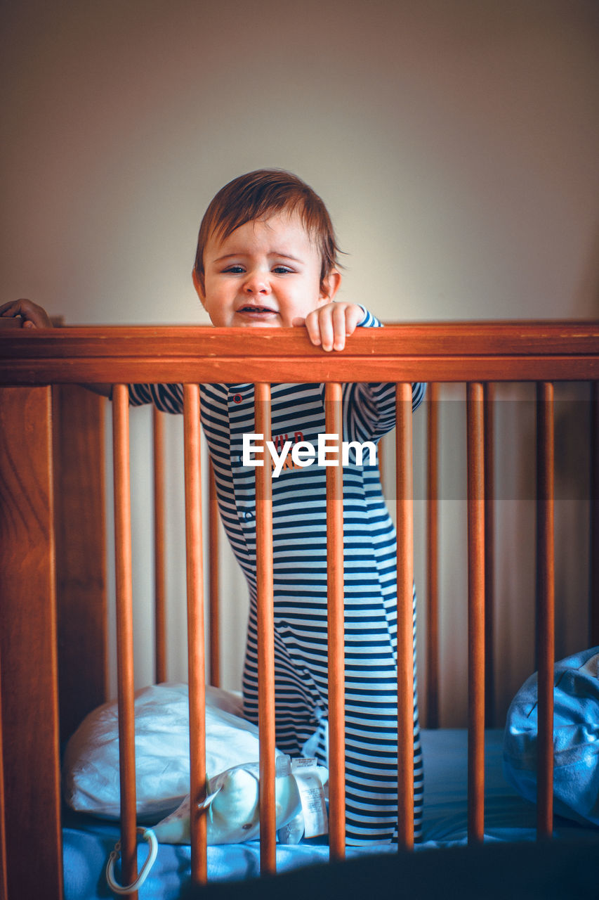 Portrait of cute baby boy standing in crib at home