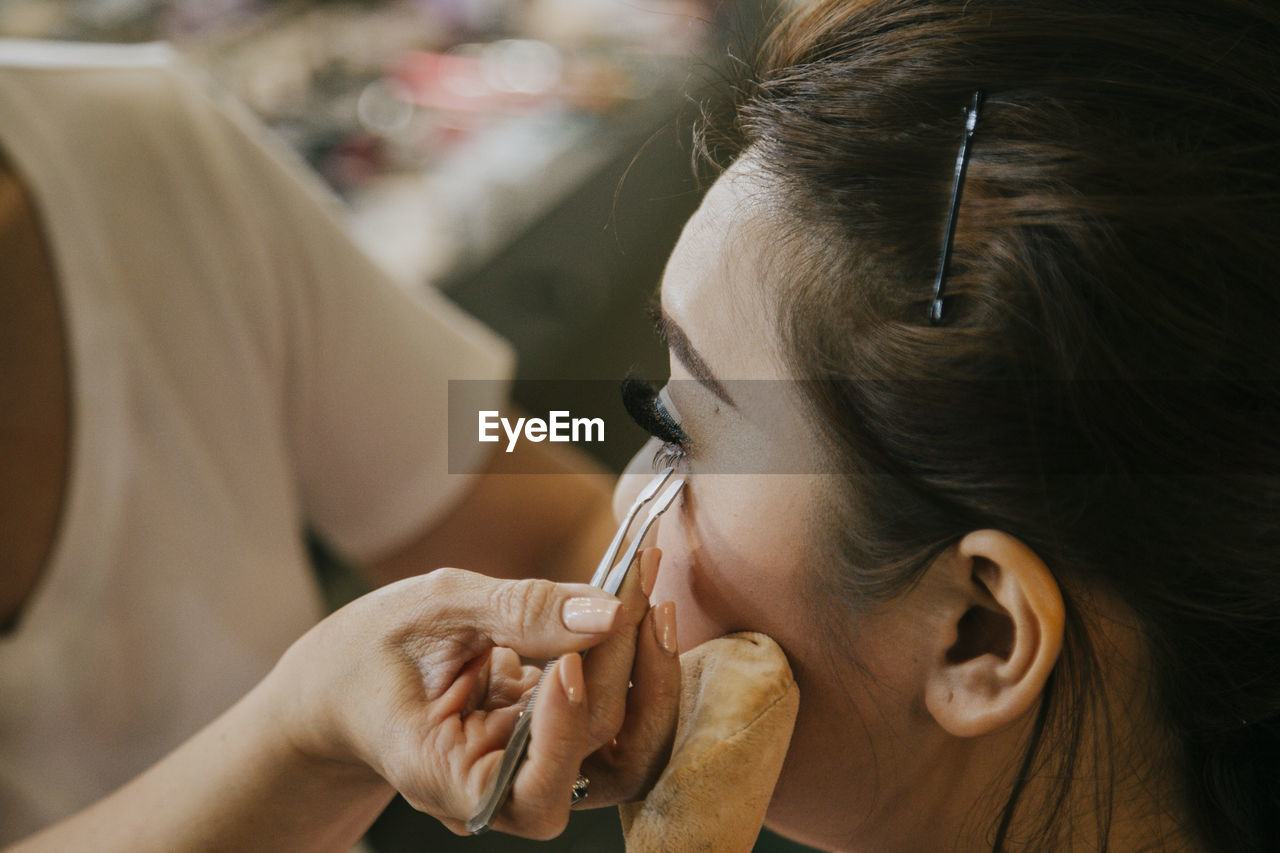 Make-up artist applying false eyelashes on young woman