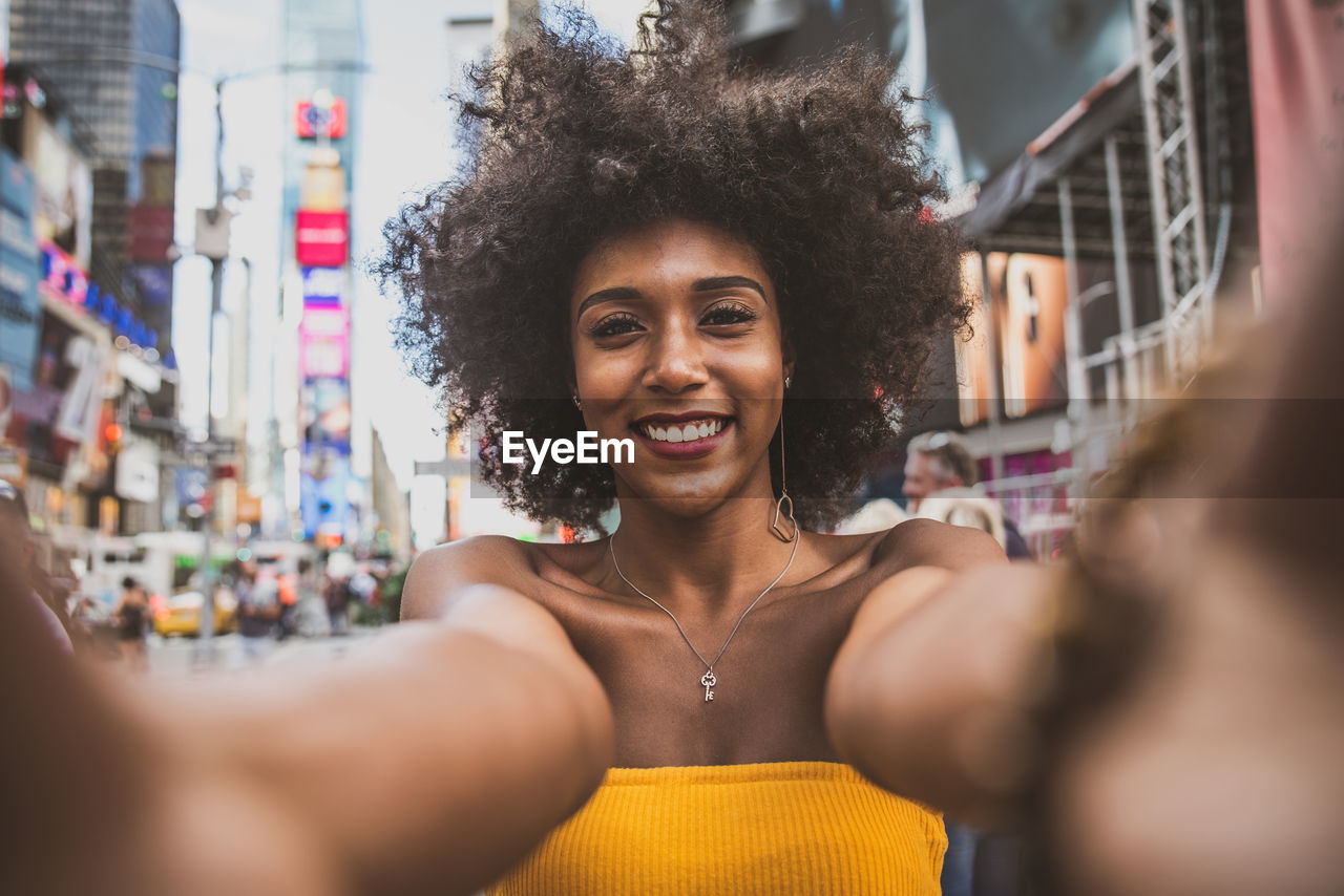 Portrait of happy young woman with afro hairstyle taking selfie on city street