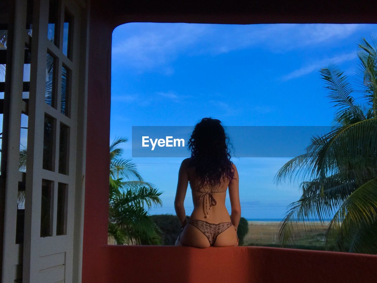 Rear view of woman sitting on wall against sky