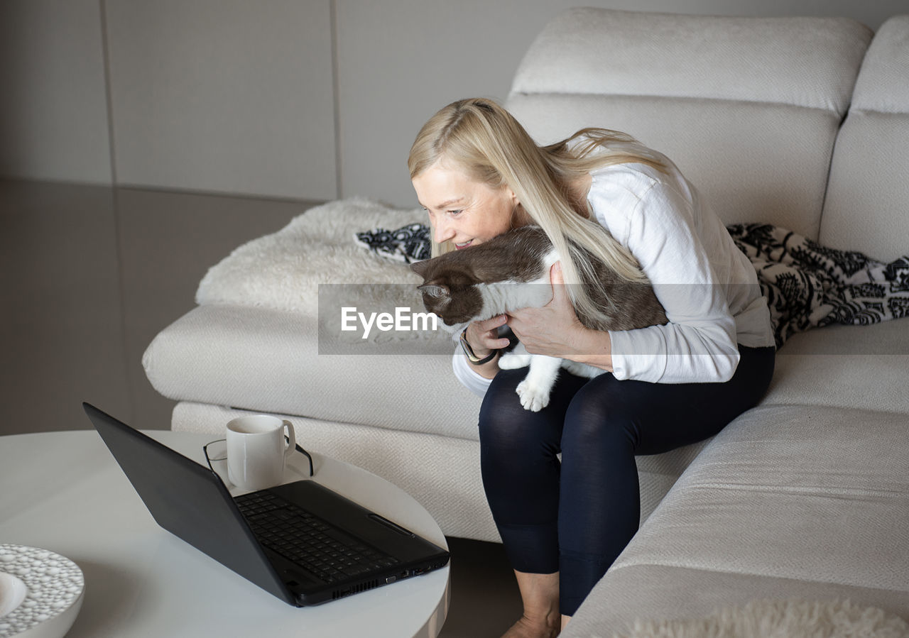 Mature woman female mother and cat using laptop and talking through video chat