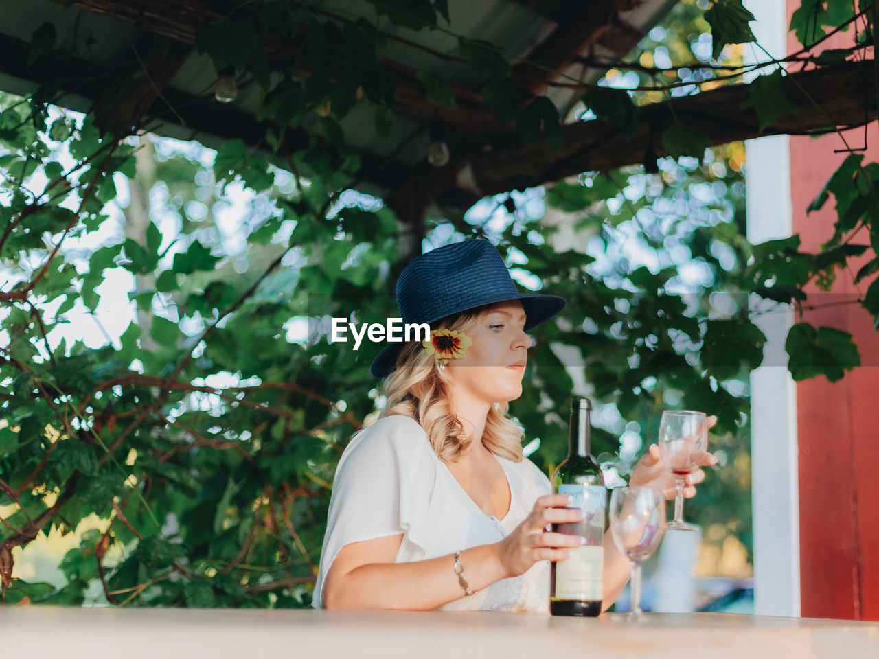 PORTRAIT OF WOMAN HOLDING HAT AGAINST TREES