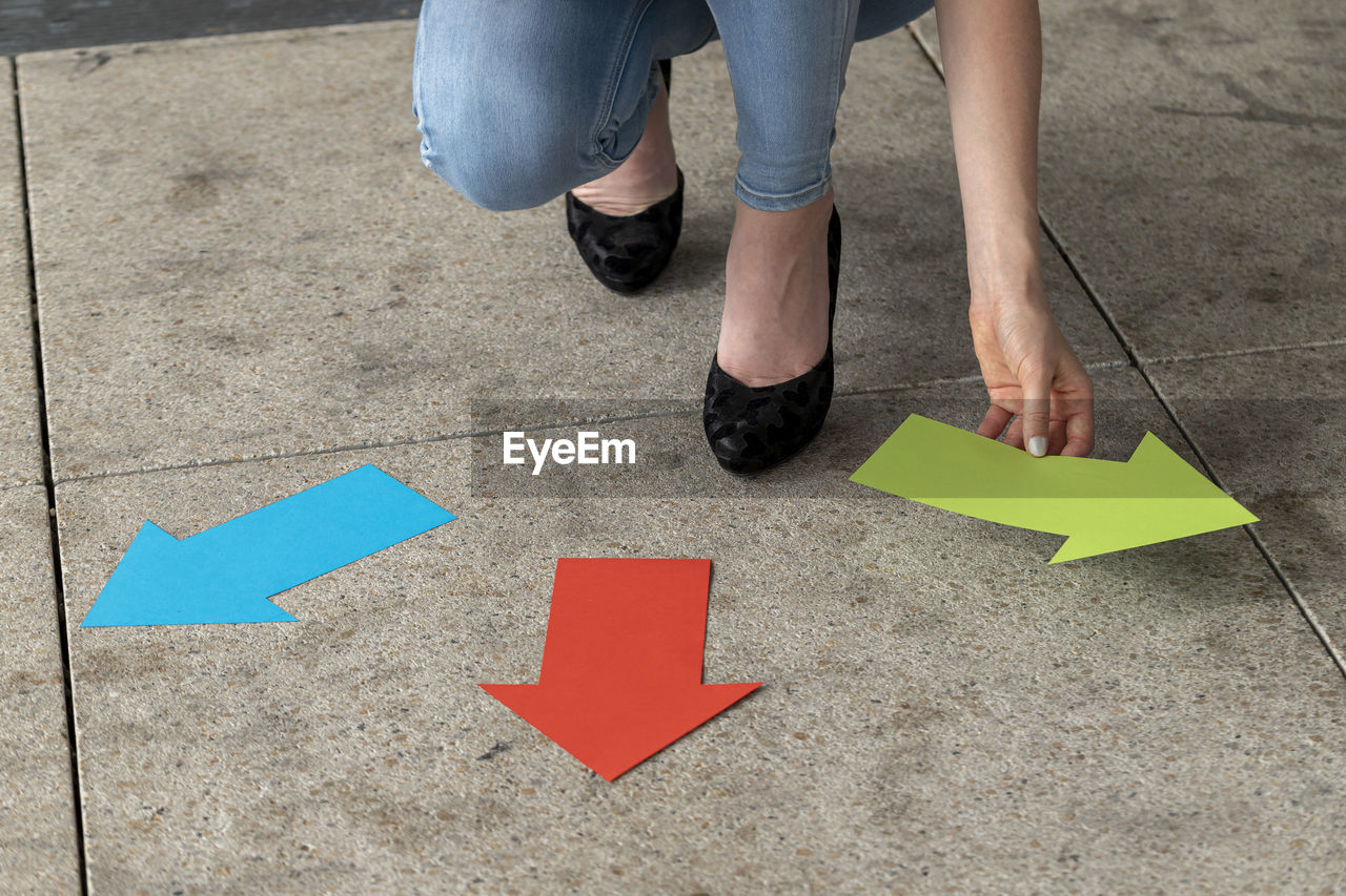 Low section of woman holding arrow symbols while crouching on tiled floor