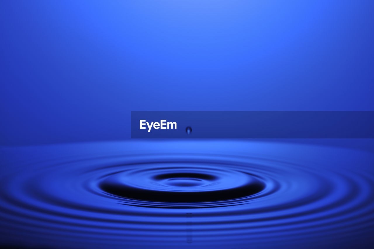 Close-up of drop falling on water against blue background