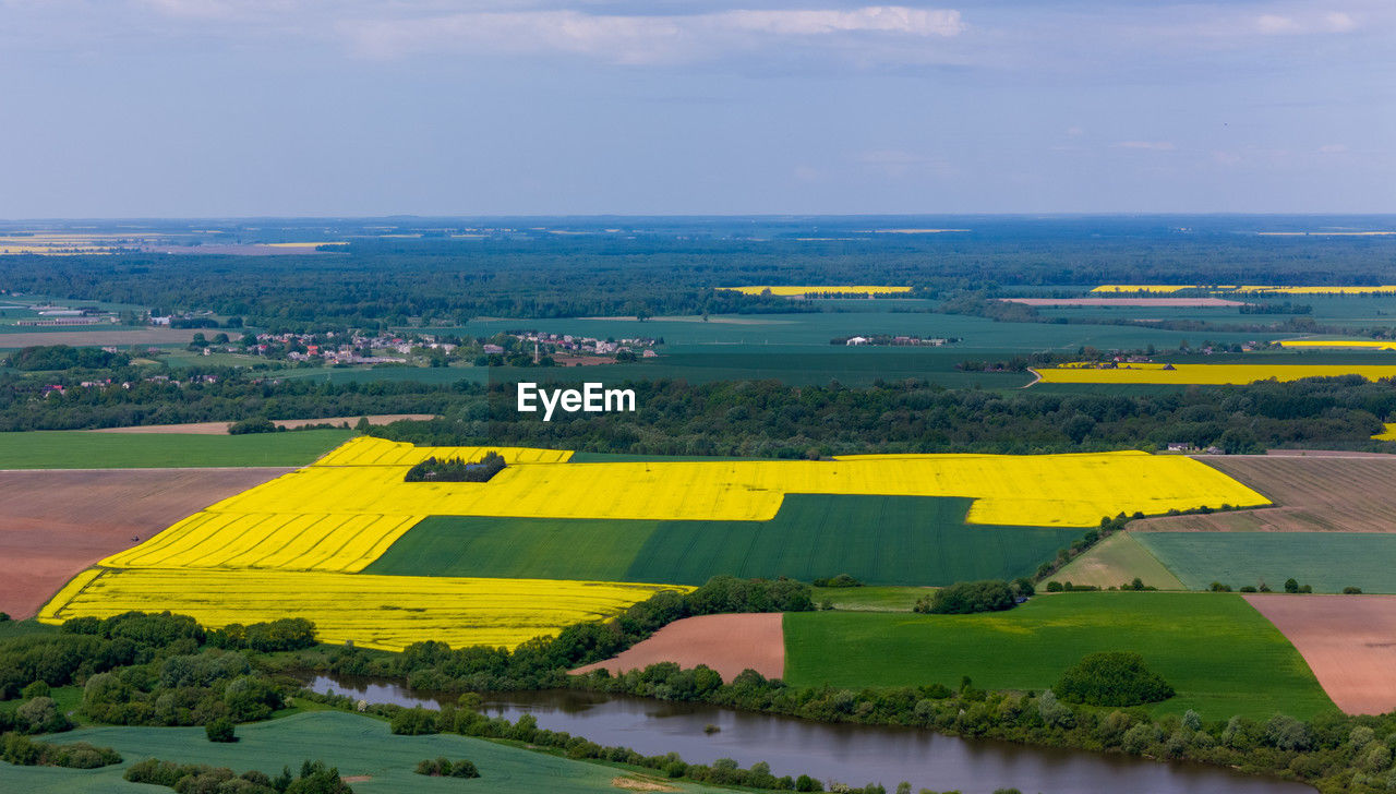 landscape, field, plain, environment, land, scenics - nature, aerial photography, horizon, nature, rural scene, water, sky, agriculture, rural area, plant, beauty in nature, farm, no people, tranquility, aerial view, tranquil scene, hill, yellow, high angle view, cloud, day, rapeseed, architecture, outdoors, green, growth, idyllic, sea, crop, travel, building, travel destinations, built structure, transportation, non-urban scene, building exterior, patchwork landscape, tree, canola, flower, grass
