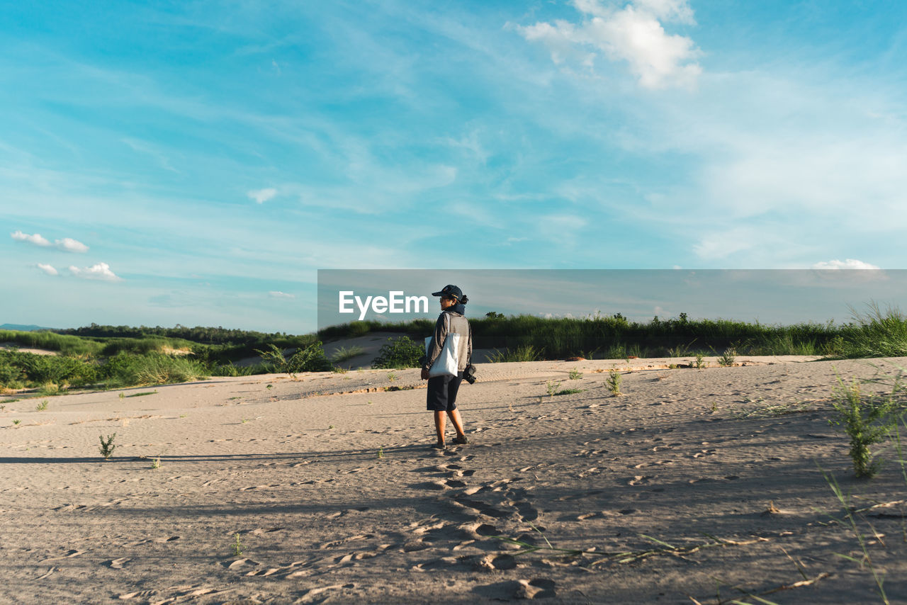 WOMAN STANDING ON LAND AGAINST SKY