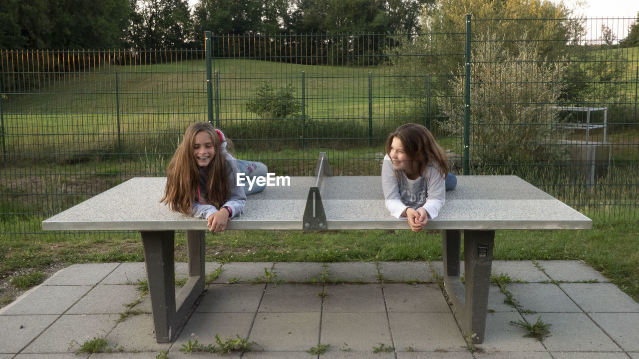 Girls lying on table tennis table at yard