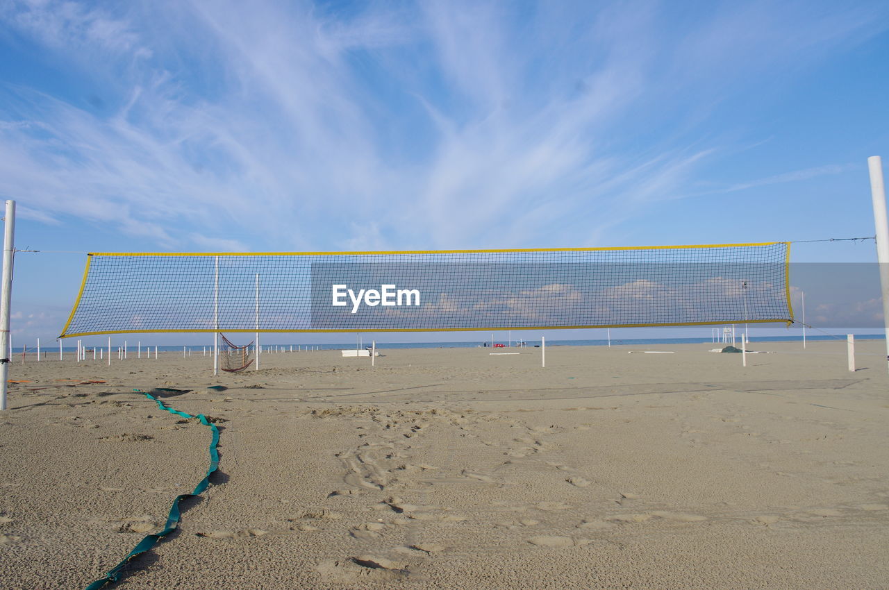 Net on sand at beach against blue sky