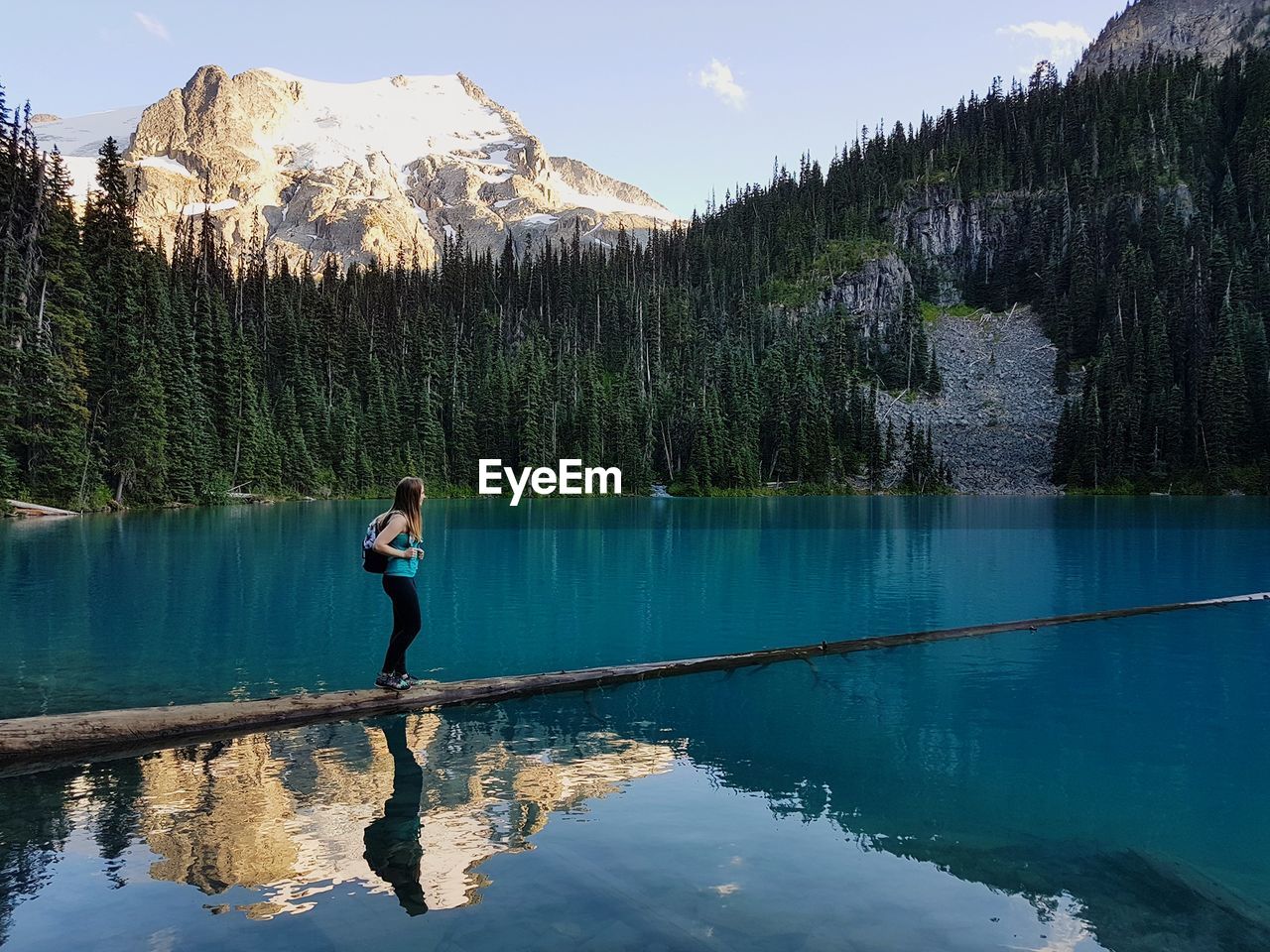 Side view of woman standing on fallen tree in lake