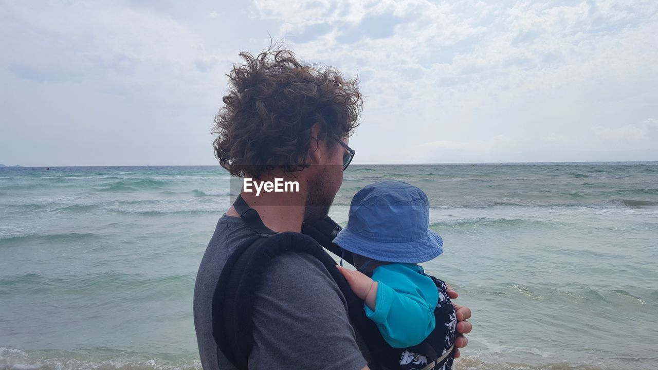 Side view of man and son at beach against sky