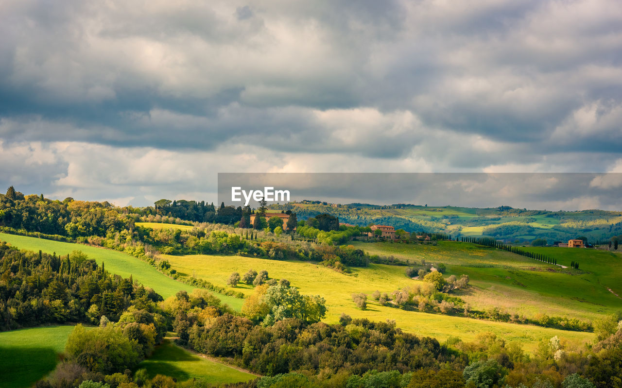 Scenic view of landscape in tuscany against cloudy sky