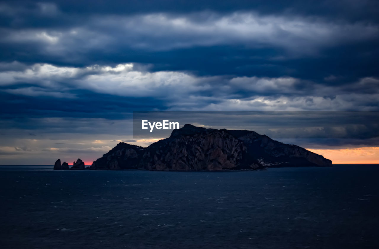 Scenic view of sea and mountains against dramatic sky