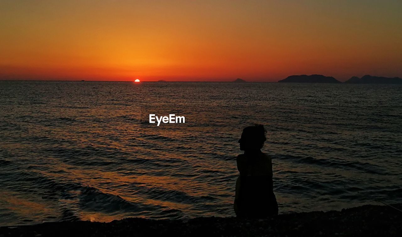 SILHOUETTE BOY STANDING ON BEACH DURING SUNSET