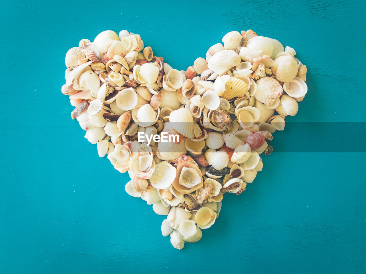 Directly above shot of heart shape made by seashells on blue table