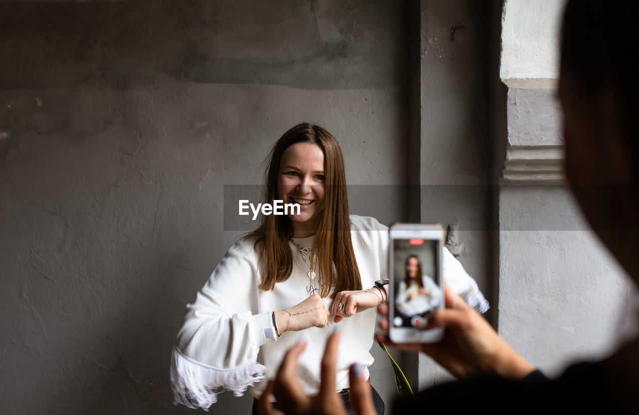 Two young women take photos and videos of each other on smartphone on a terrace