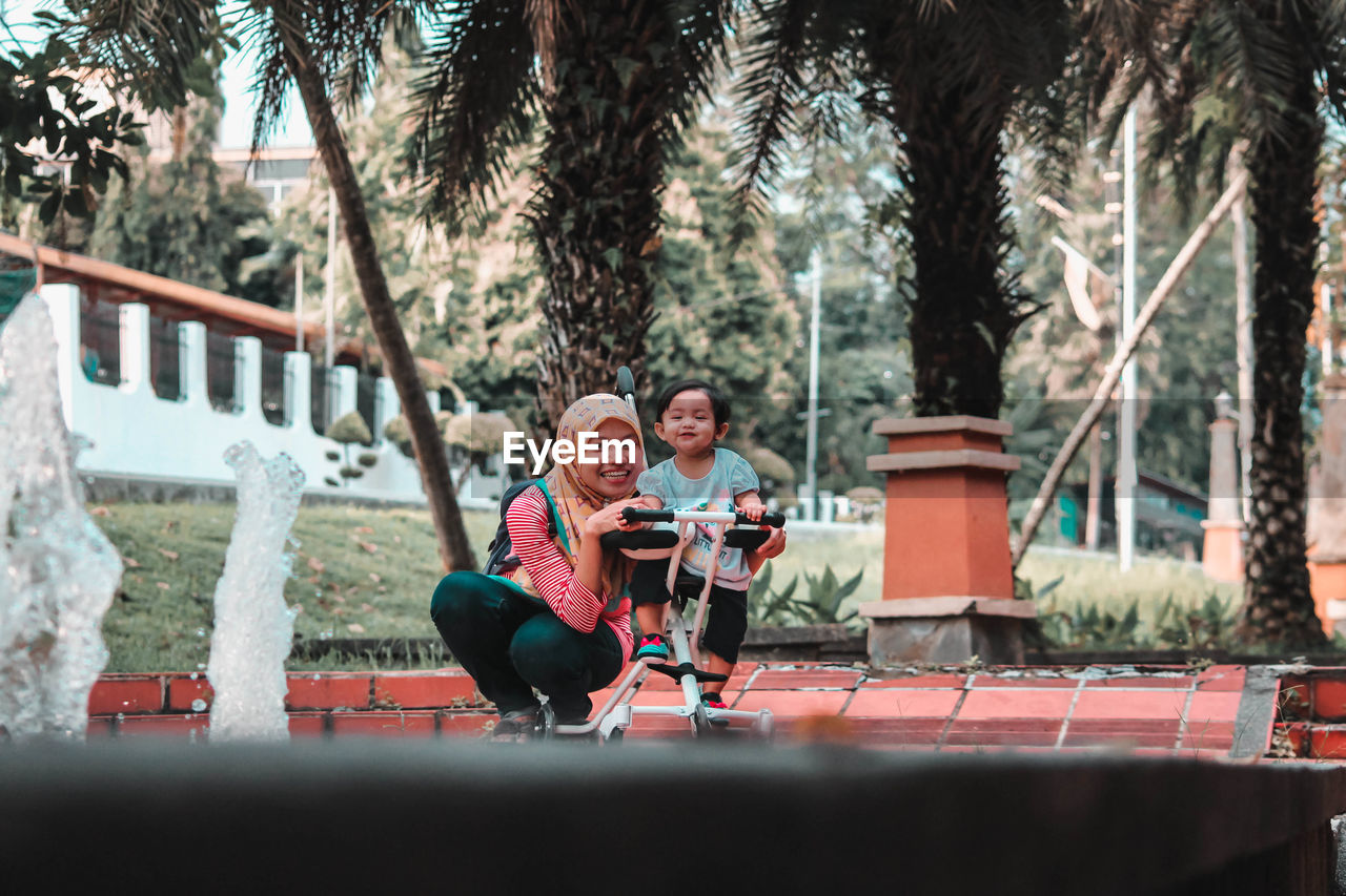 Portrait of smiling woman with daughter on toy scooter playing in park