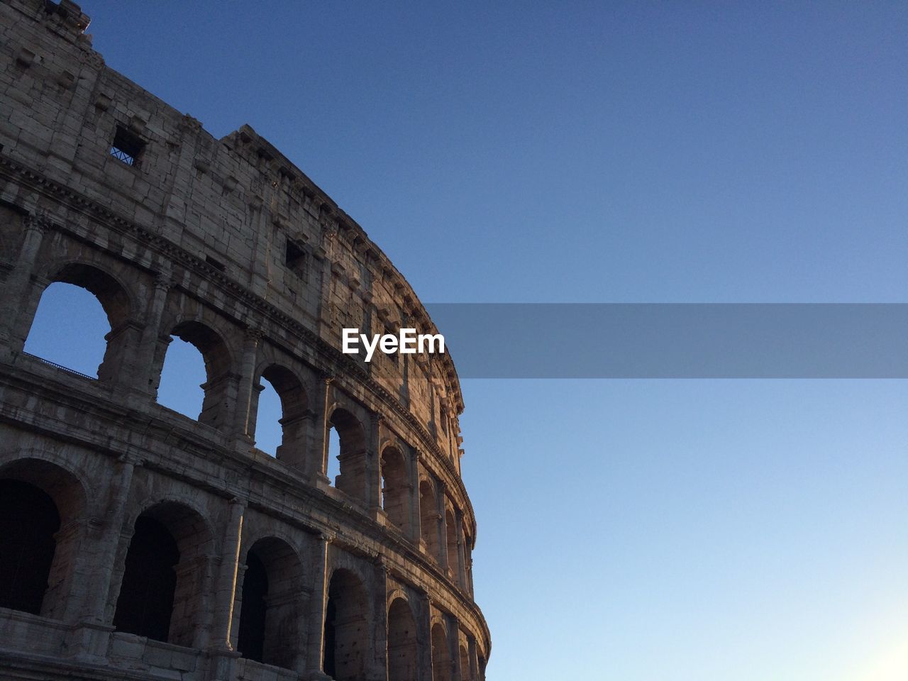 Low angle view of coliseum against clear blue sky