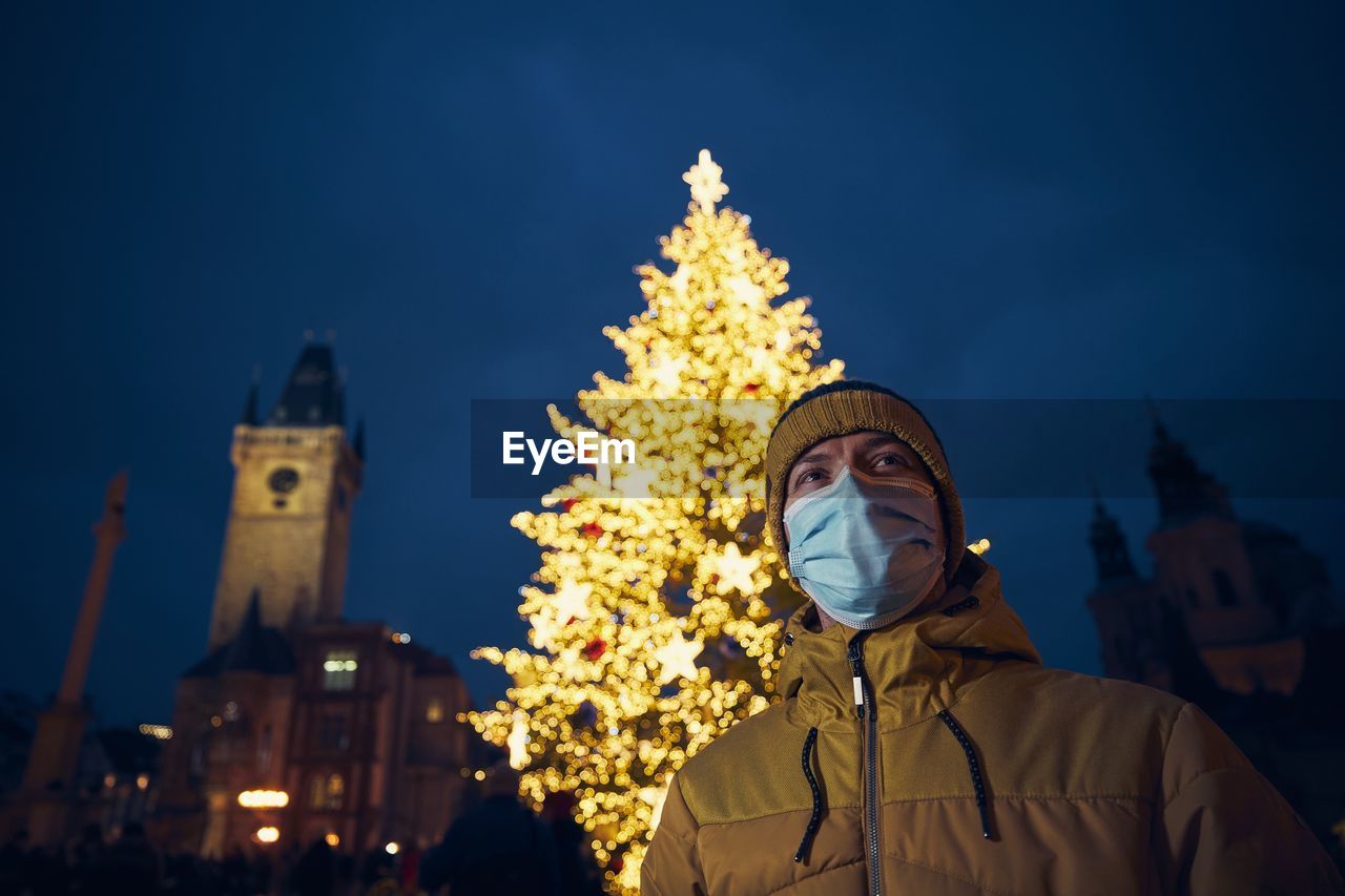 Low angle of man against illuminated christmas tree at night