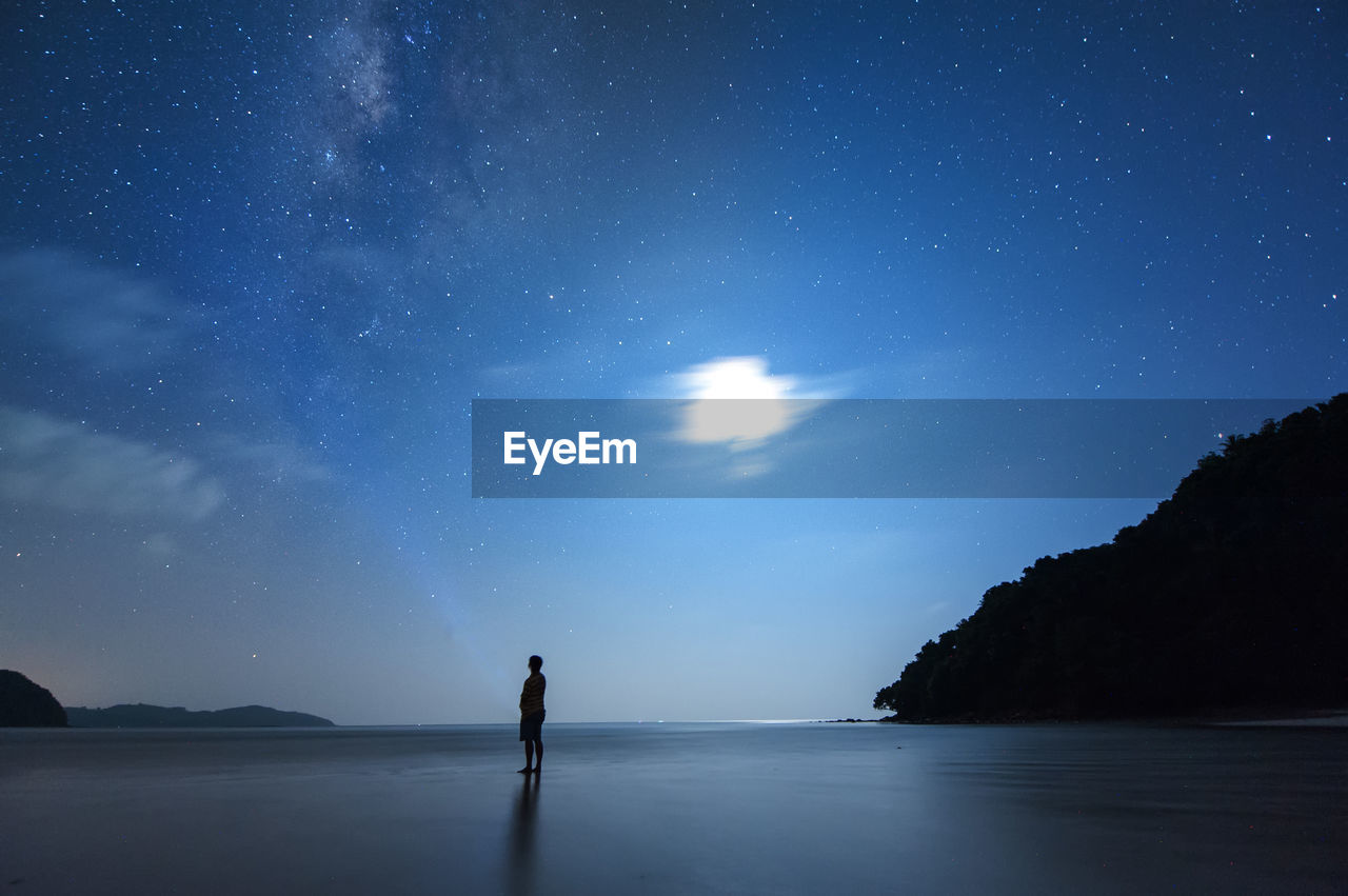 Silhouette man standing at beach against star field at night