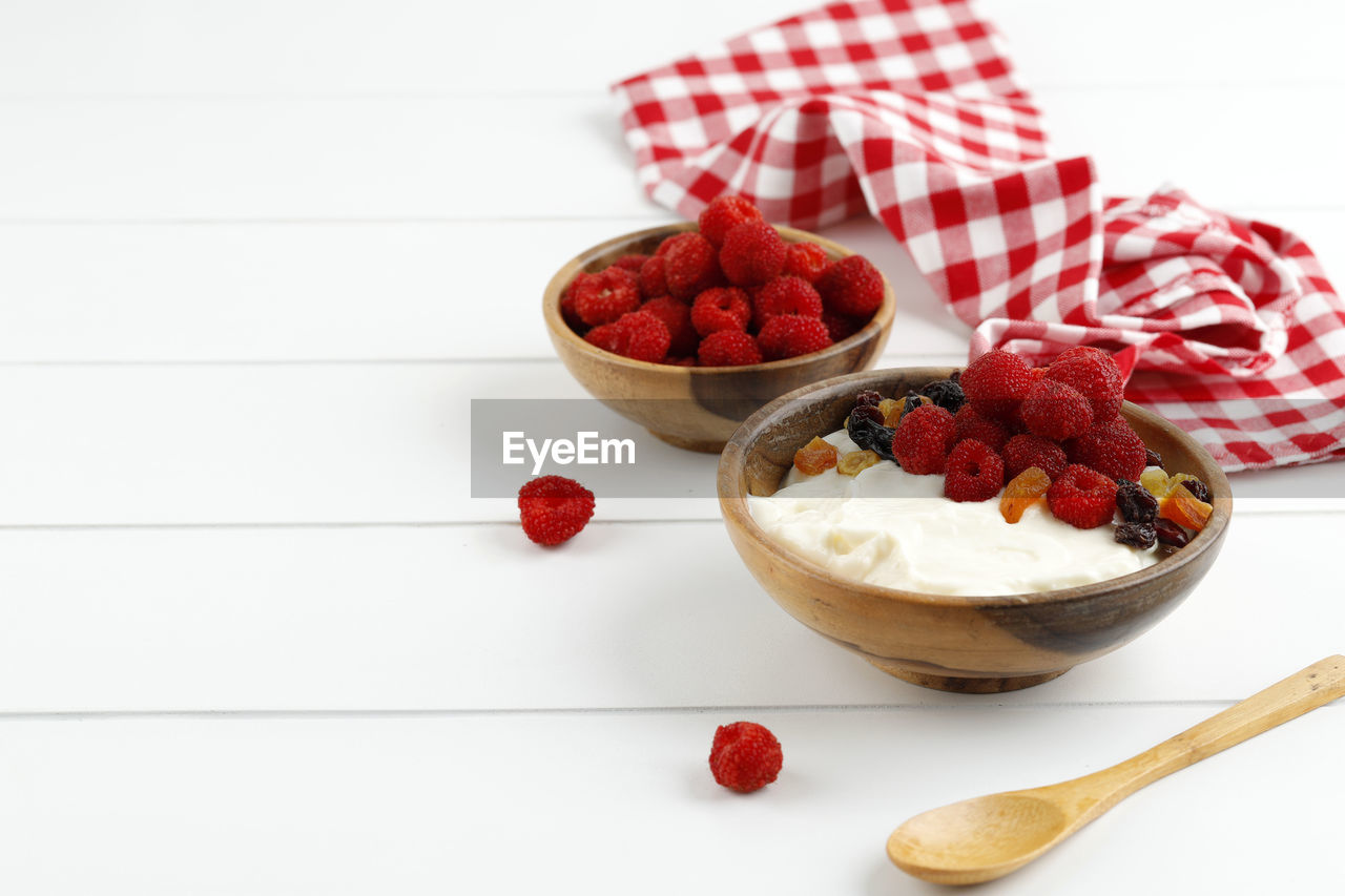 Homemade greek yogurt with raspberry and dried fruit, copy space for text on white background