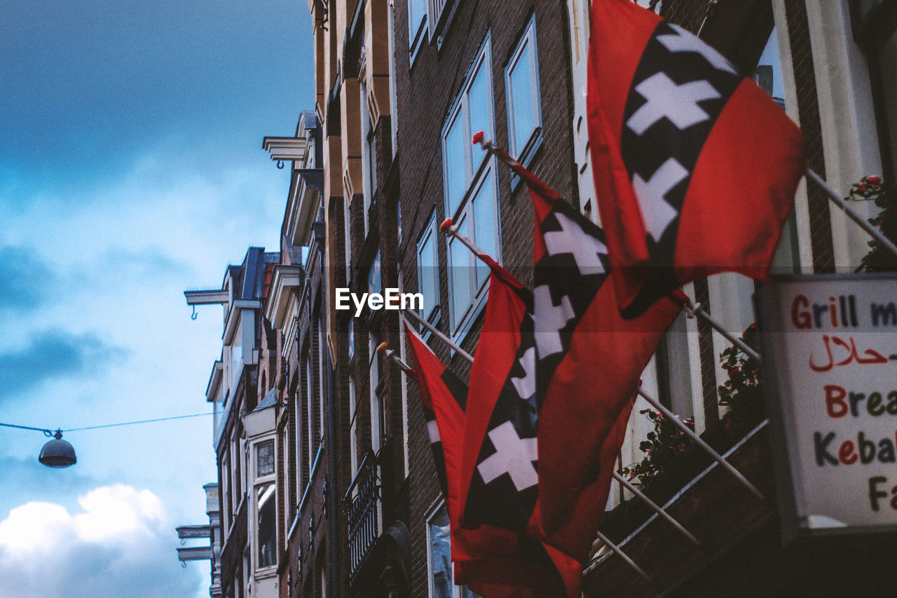 sky, flag, architecture, cloud, low angle view, patriotism, built structure, building exterior, nature, no people, communication, text, city, day, sign, outdoors, hanging, red