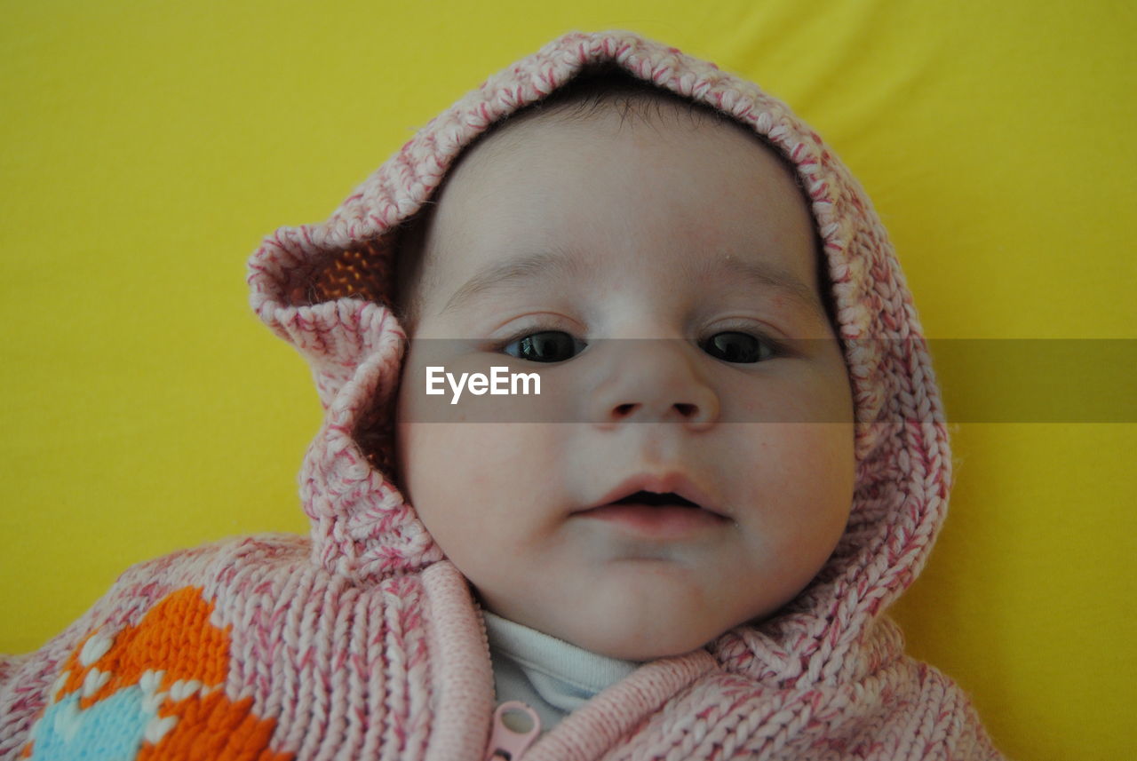 Cute baby girl wearing knitted warm clothing lying on bed