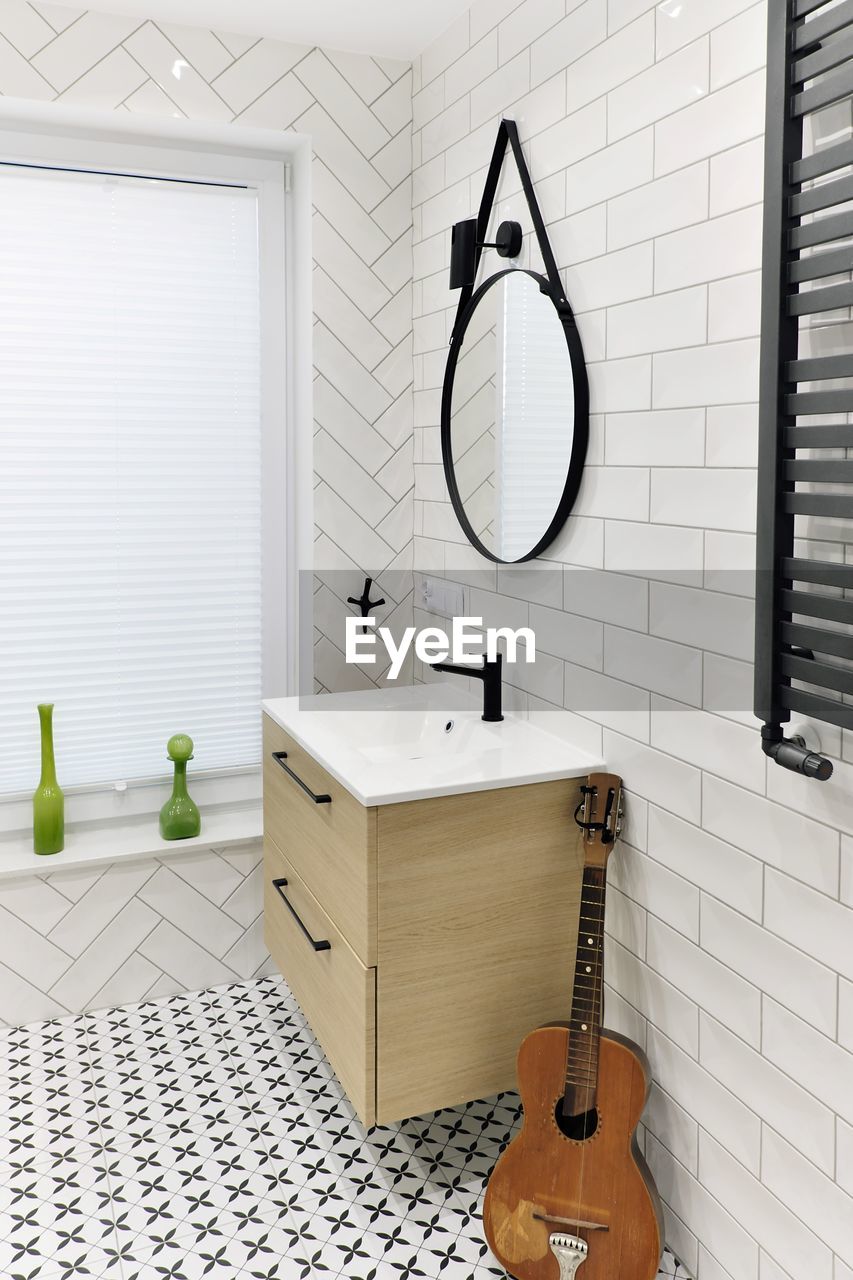 Modern bathroom washbasin with black tap, round mirror and black and white  tiles and old guitar