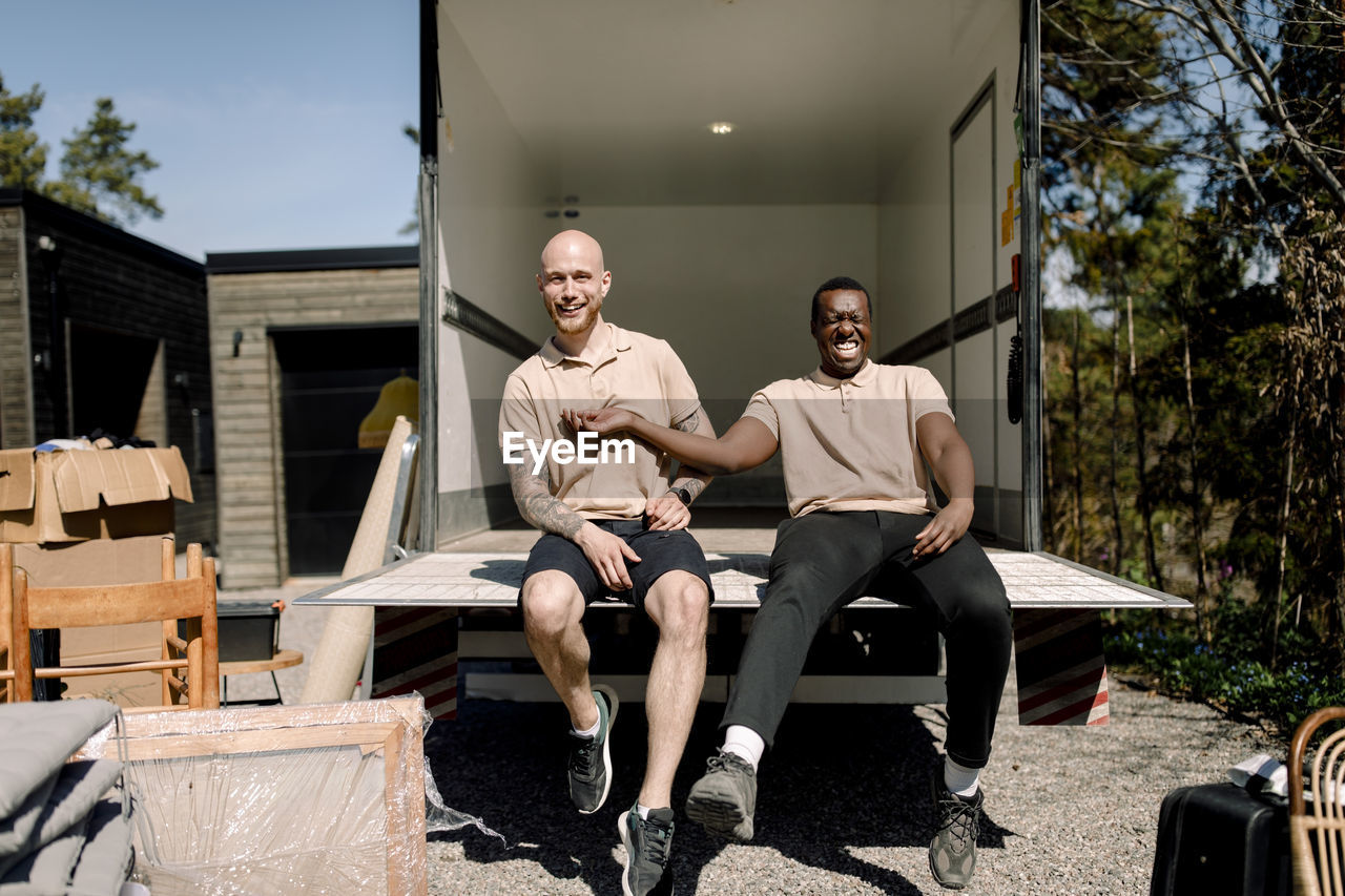 Portrait of smiling multiracial movers sitting in trunk of delivery truck