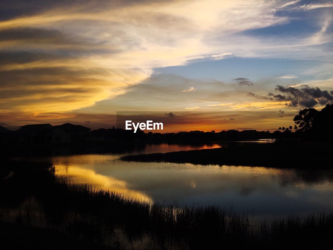 Scenic view of lake against cloudy sky during sunset