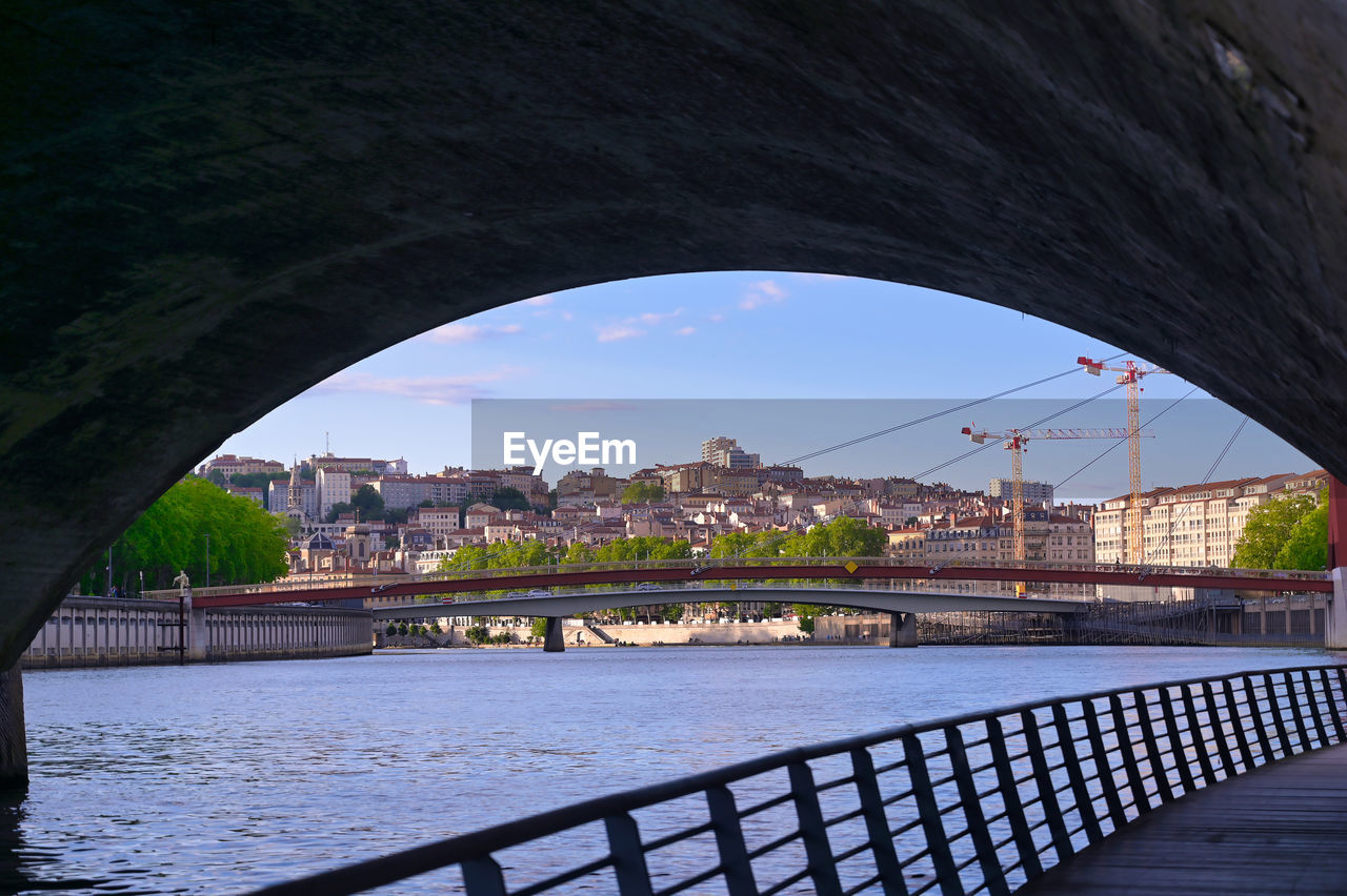 ARCH BRIDGE OVER RIVER SEEN THROUGH CITY BUILDINGS