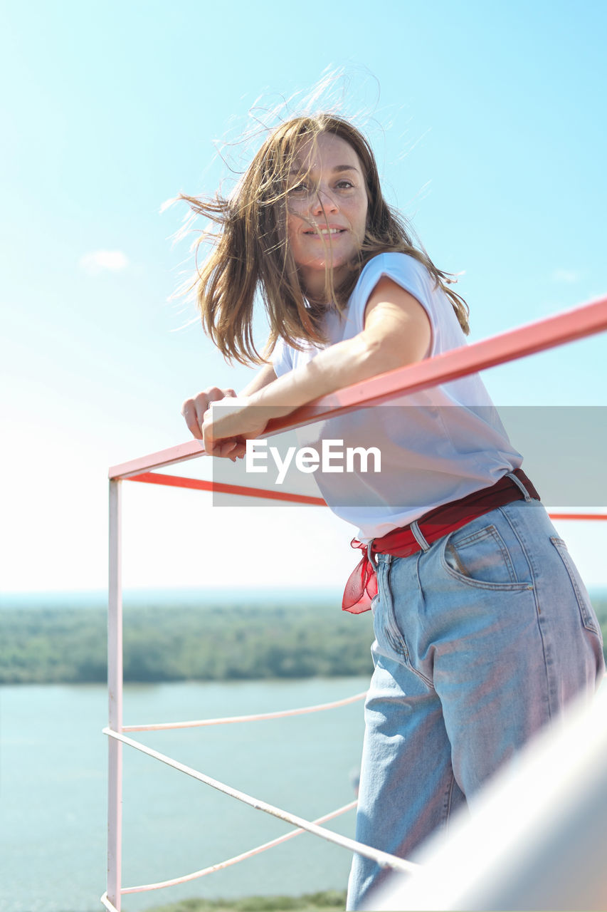 Young woman standing over river bank on a balcony or terrace enjoying landscape view. wind blowing 