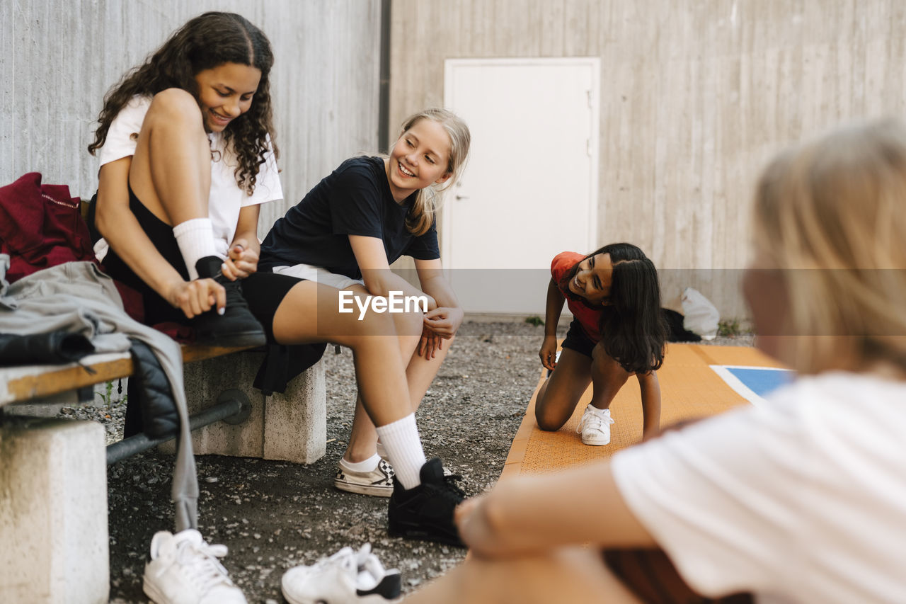 Smiling girl tying shoelace while sitting with female friends in sports court