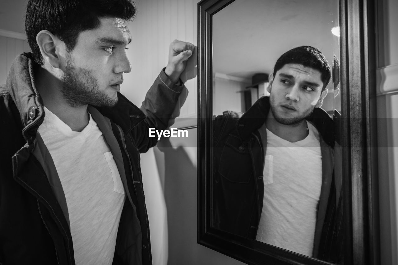 Young man looking at his reflection in mirror at home