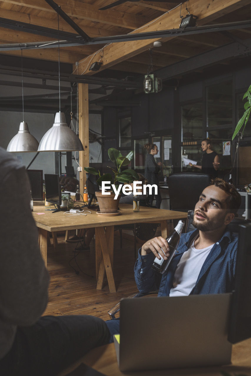 Businessman with beer talking to colleague at workplace