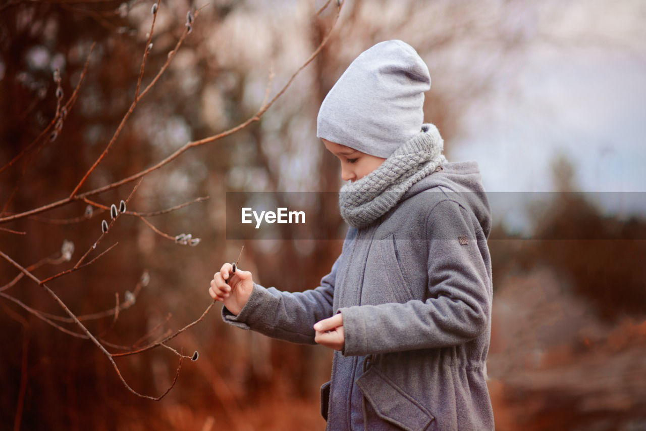 Side view of boy standing near the willow tree and touching the twig 