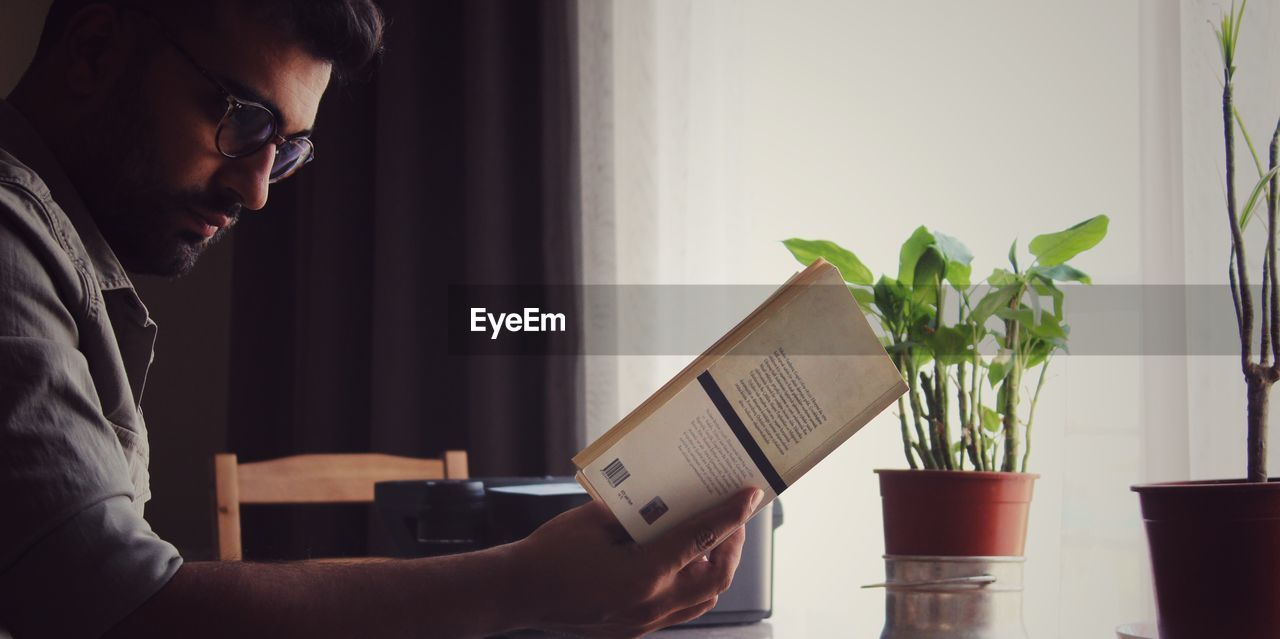 Side view of young man reading book at home