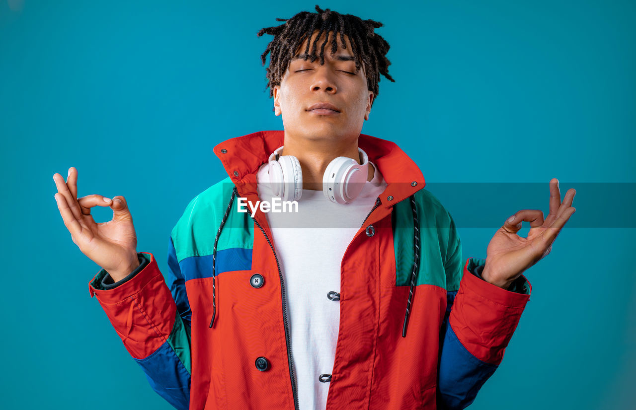 one person, colored background, studio shot, blue, portrait, blue background, clothing, waist up, front view, men, technology, young adult, indoors, standing, gesturing, communication, person, emotion, adult, child, red, looking at camera, wireless technology, fun, copy space, smartphone, mobile phone, portable information device, headphones, childhood