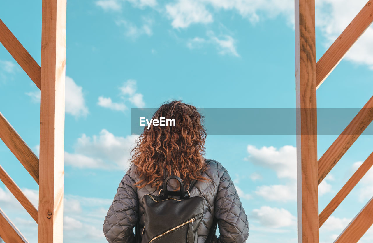 Rear view of mature woman with backpack standing against blue sky